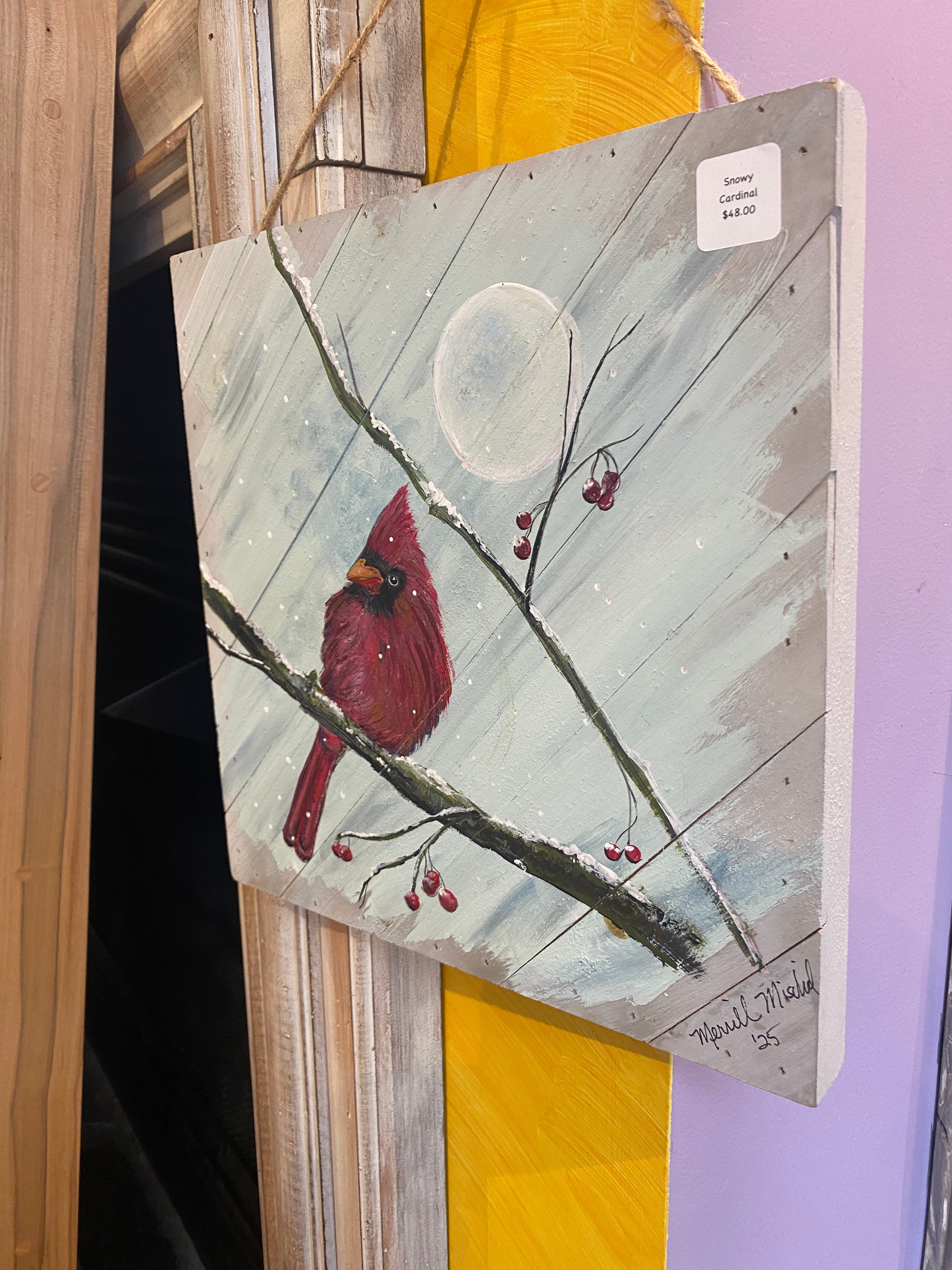 Painting of a cardinal bird on a branch with berries and a moon in the background, displayed against a purple wall.