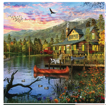 Load image into Gallery viewer, Cozy cabin by a lake with mountains in the background during sunset.

