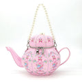 Pink teapot-shaped handbag with floral patterns and a pearl handle on a white background