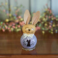 Decorative Easter bunny figurine with a light purple base on a wooden surface.