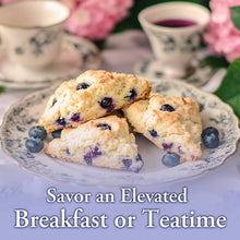 Load image into Gallery viewer, Blueberry scones on a decorative plate with teacups and flowers in the background.
