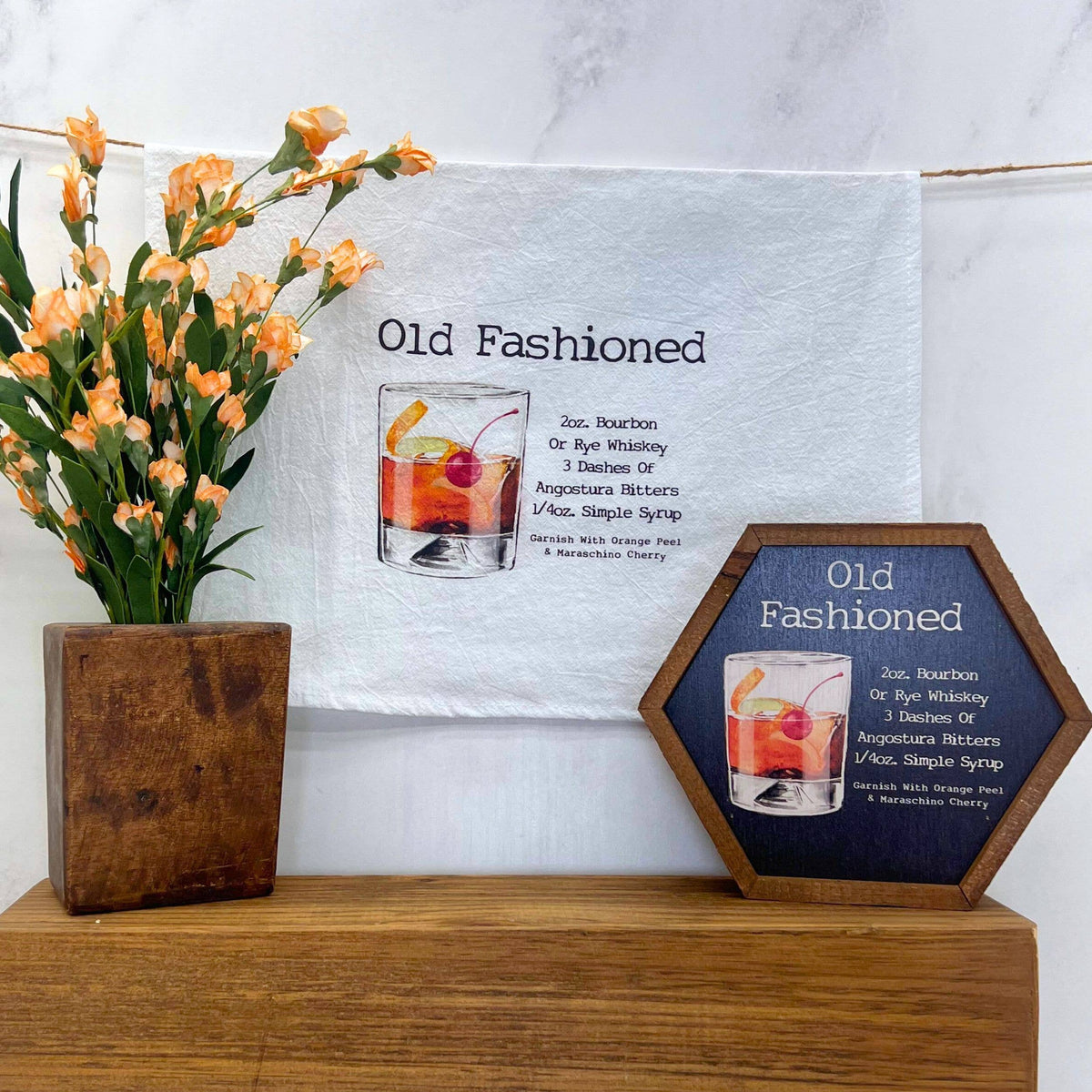 Decorative signs with 'Old Fashioned' cocktail recipe and illustration on a wooden surface with flowers.